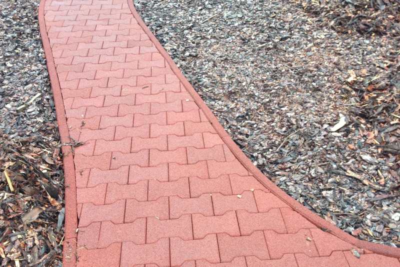 Ein roter Weg mit WARCO-Knochensteinen zieht sich geschwungen durch einen Garten.