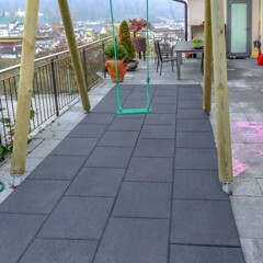 Ein Teilbereich einer aus Betonplatten angelegten Terrasse wurde zum Aufstellen einer Schaukel genutzt. Der Bereich unter der Schaukel ist durch Fallschutzplatten abgesichert